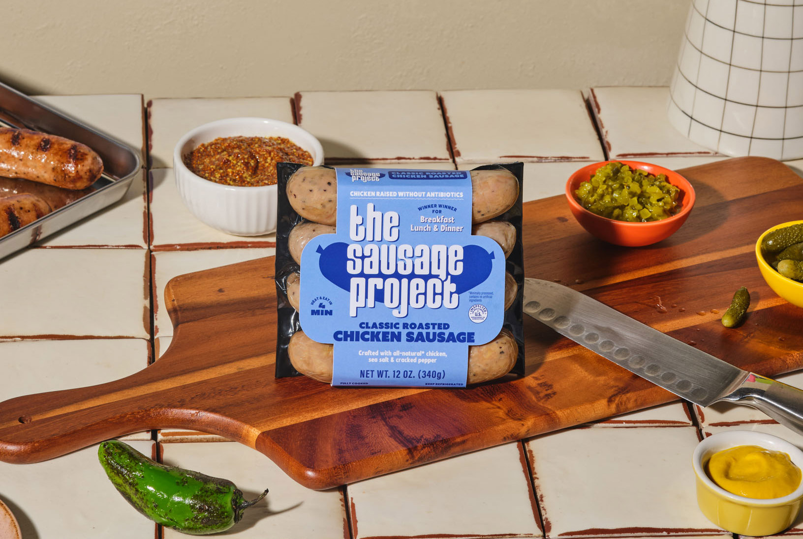 The Sausage Project Classic Roasted Chicken on a cutting board with sauces and peppers.