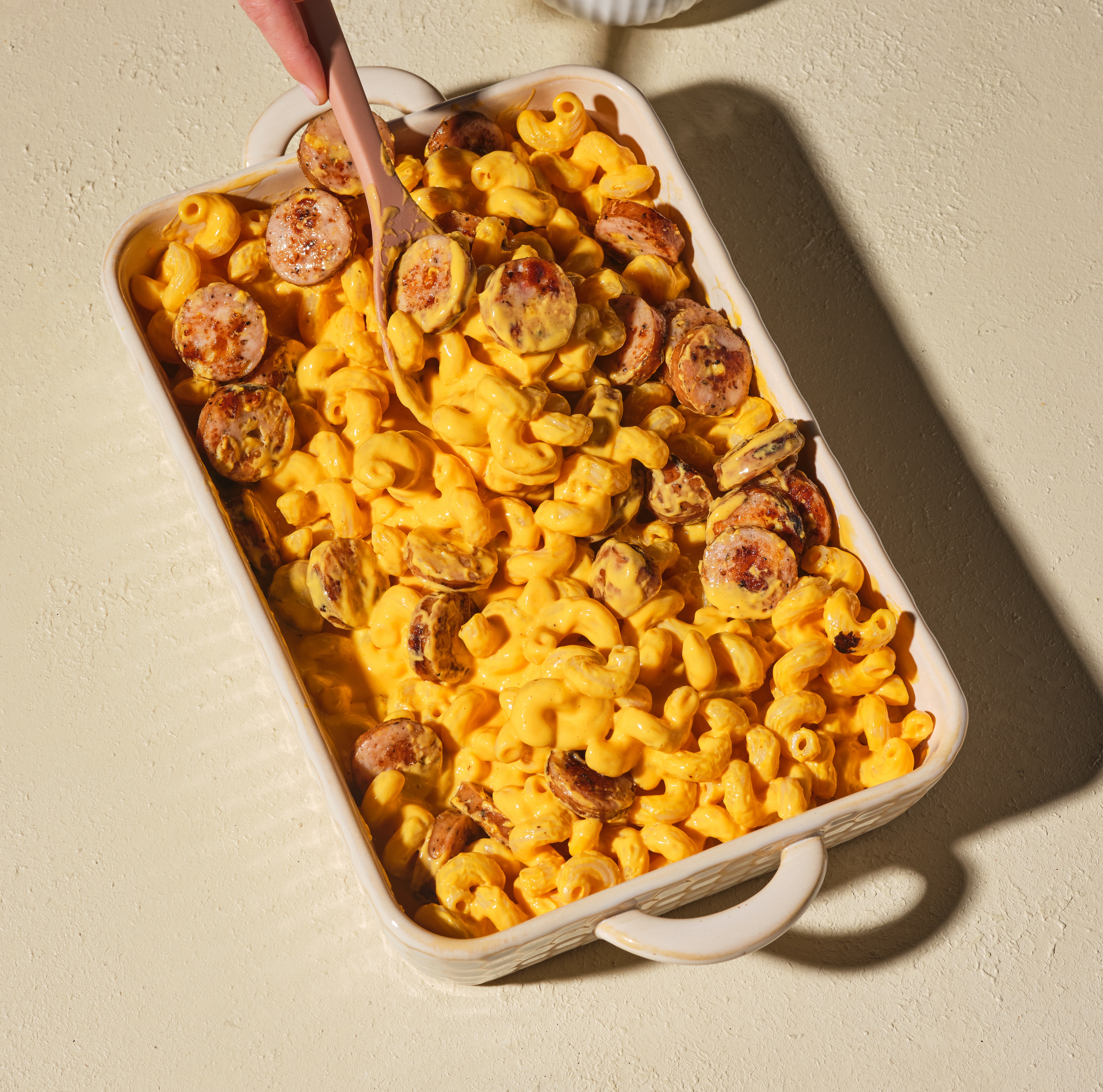 Baked mac and cheese with The Sausage Project Melty Cheddar Chicken Sausage coins and buttery cracker topping in a casserole dish.