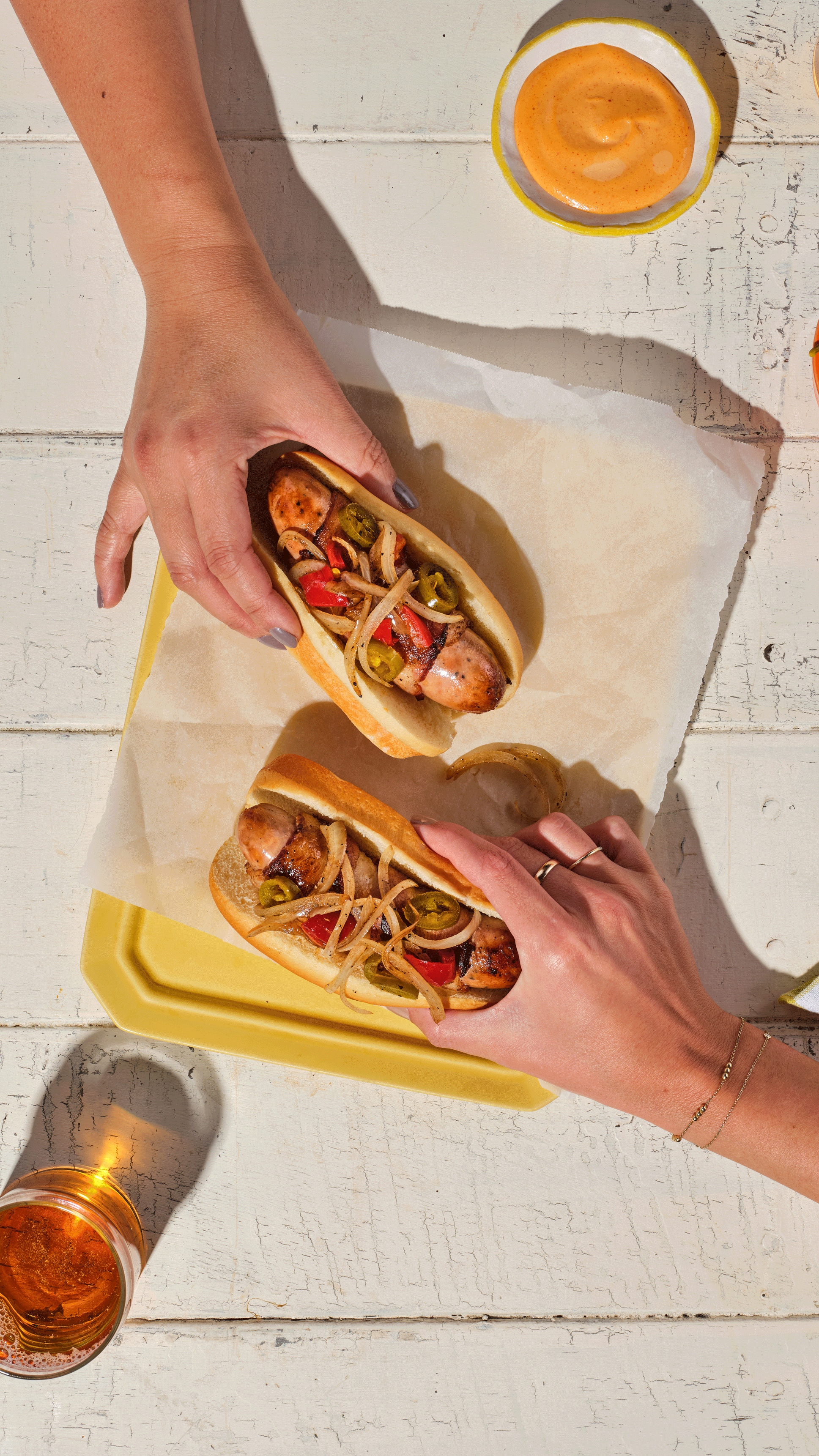 Bacon-wrapped cheddar chicken sausage topped with grilled peppers and onions on a toasted bun, served with a side of spicy gochujang aioli.