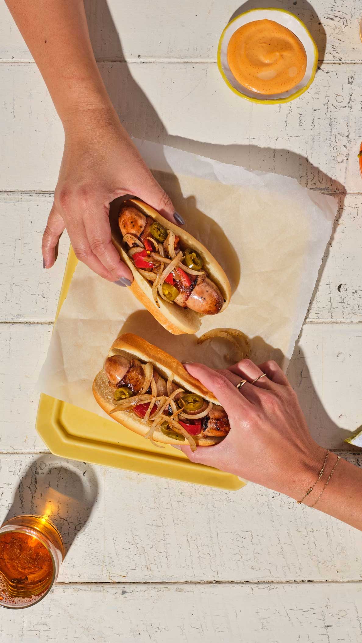 Hands reaching for delicious bacon-wrapped L.A. street dogs made with The Sausage Project's Melty Cheddar Chicken Sausage.