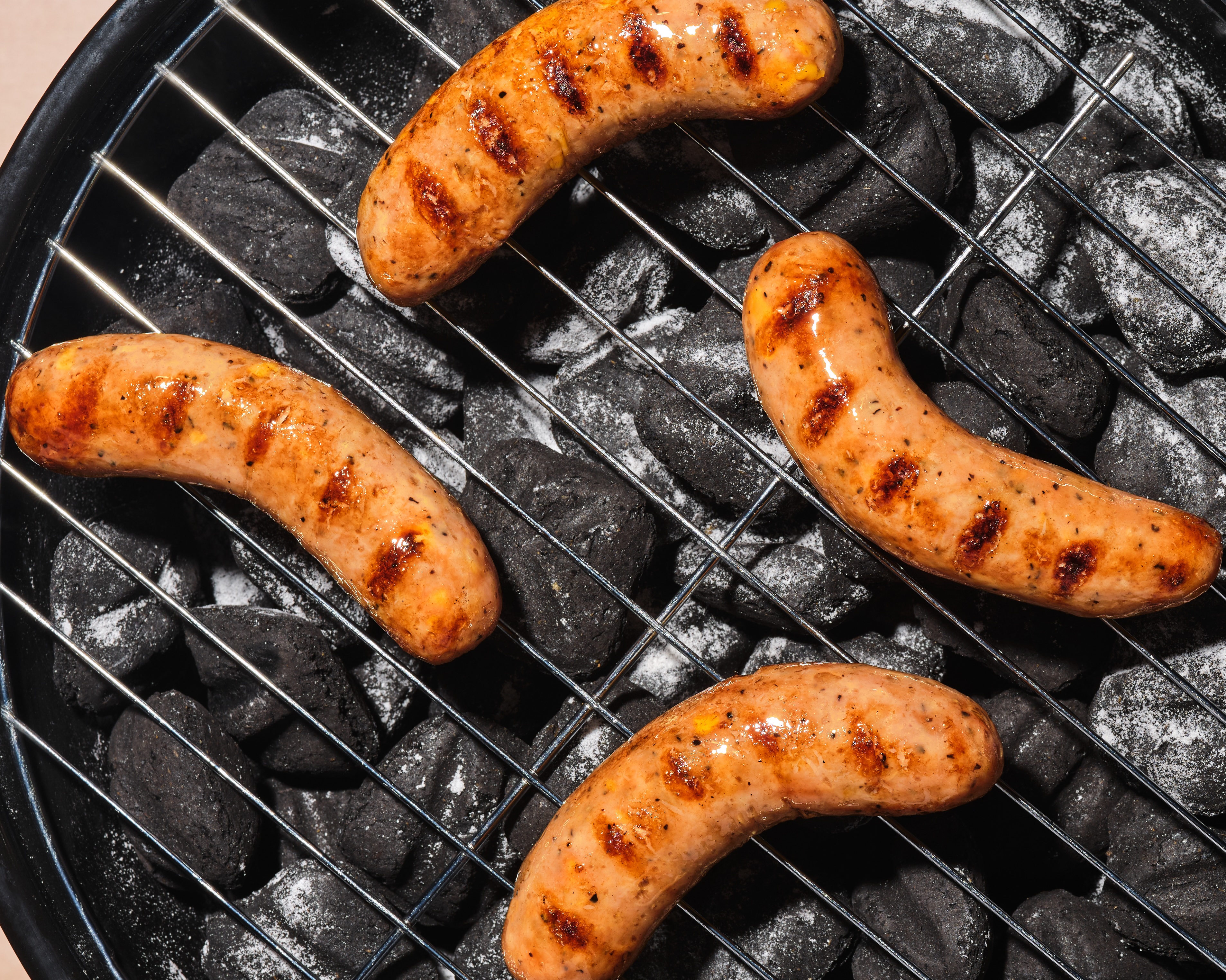 The Sausage Project chicken sausages glistening as they heat up on a charcoal grill.