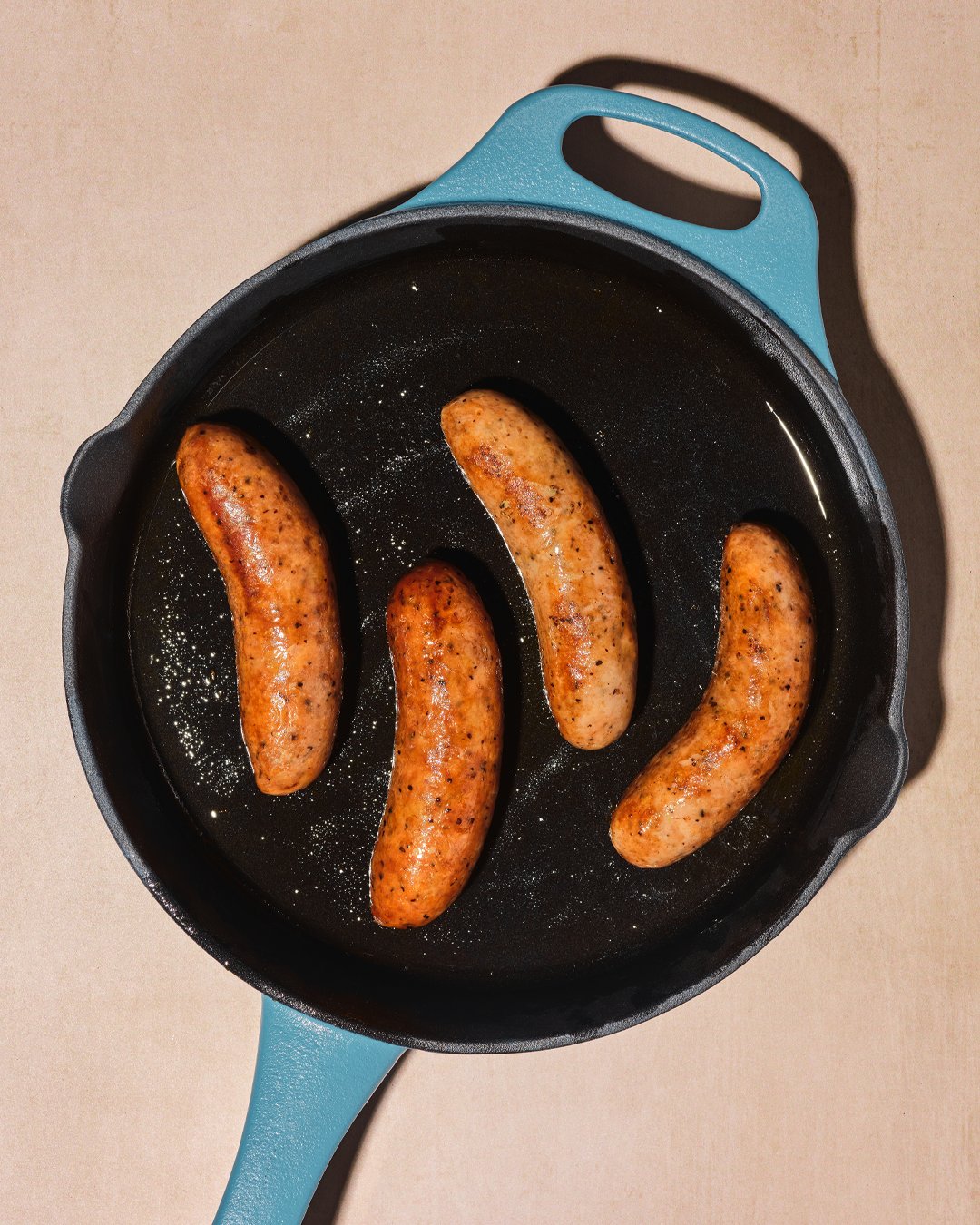 A close-up of The Sausage Project chicken sausage sizzling in a cast-iron pan.