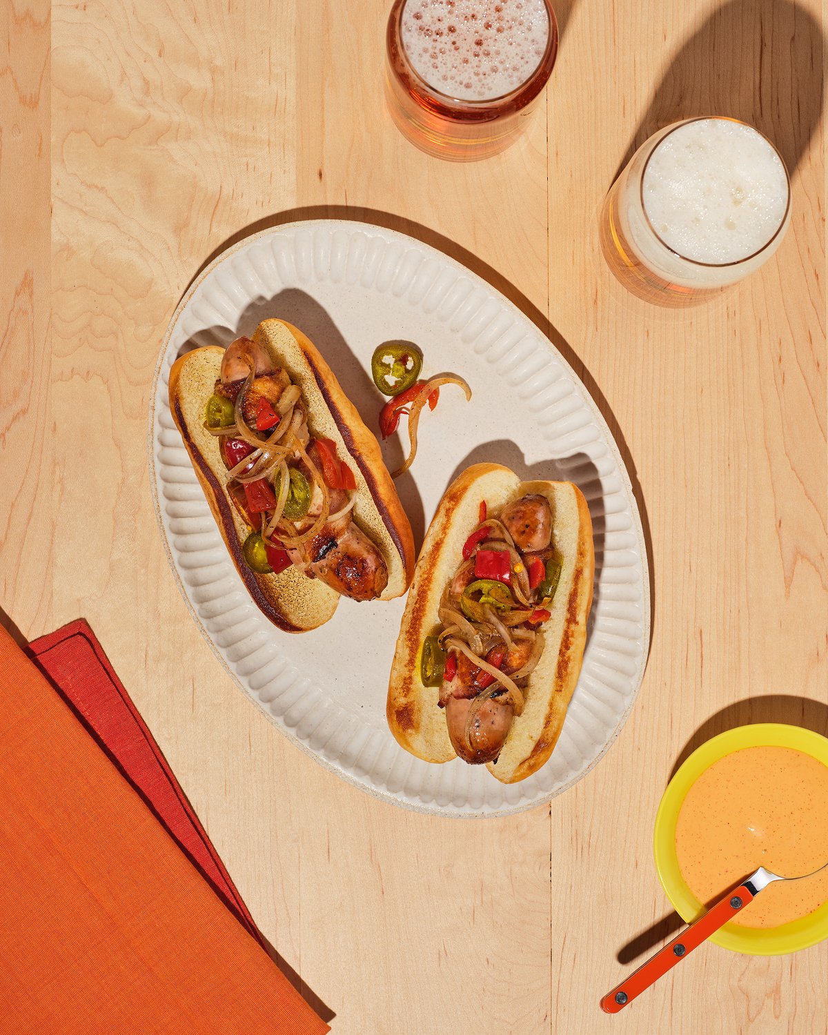 A pair of bacon-wrapped L.A street dogs made with The Sausage Project Melty Cheddar sausages, grilled onions and peppers, and served with ice-cold beer.