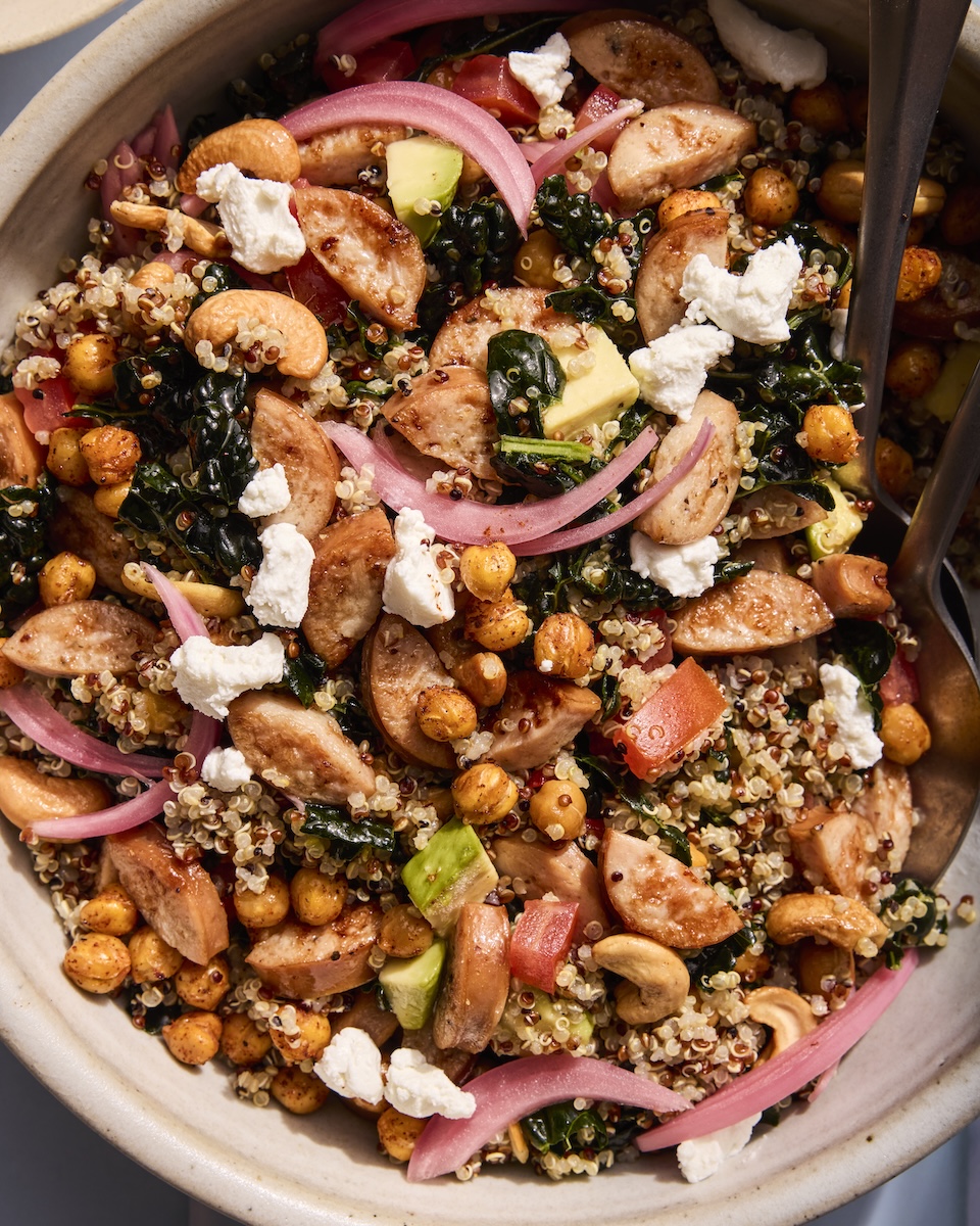 A detailed closeup of a tasty grain bowl filled with chicken sausage, quinoa, chickpeas, and avocado.