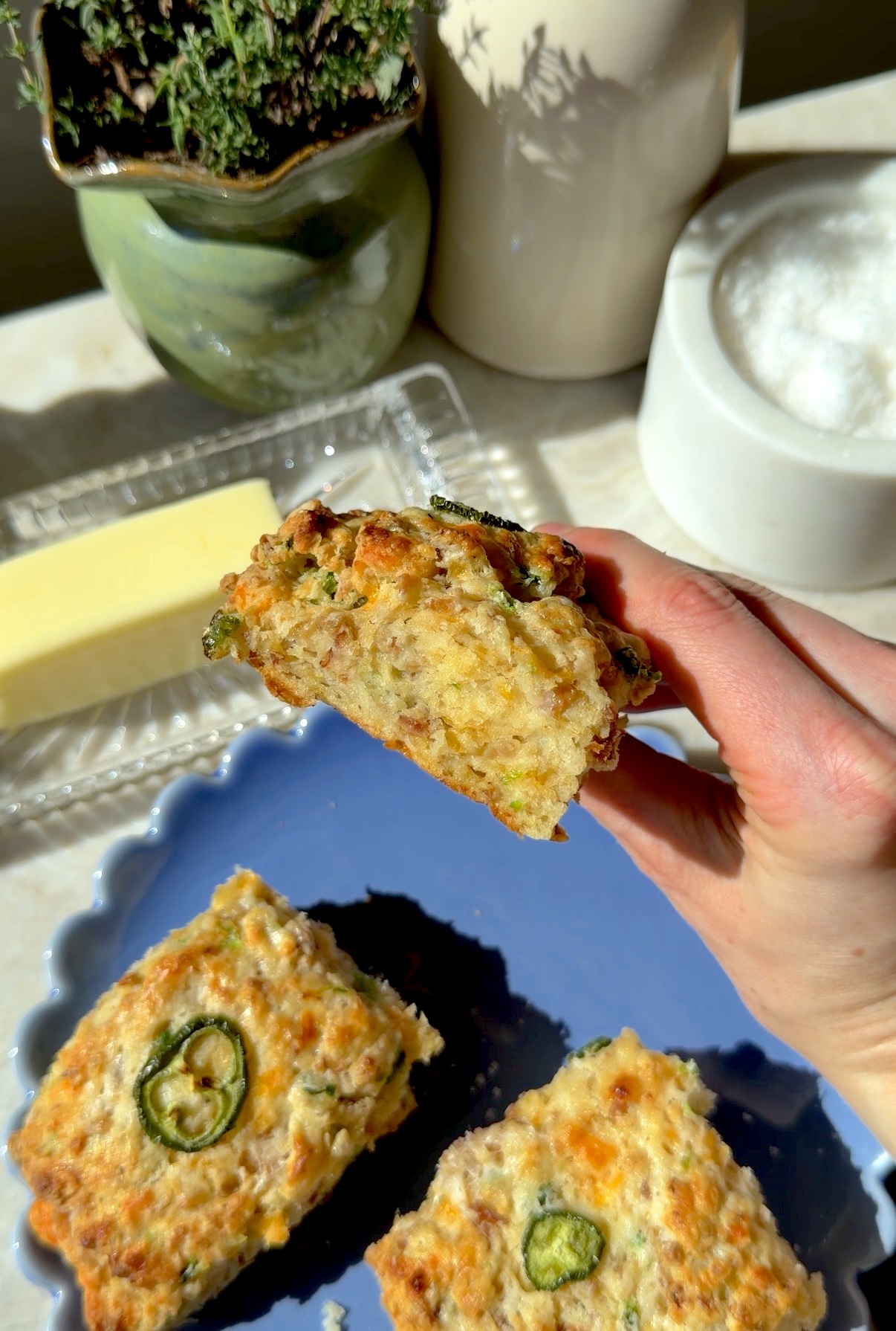 A close-up of a hand holding a hot Jalapeno Cheddar Chicken Sausage Biscuit.