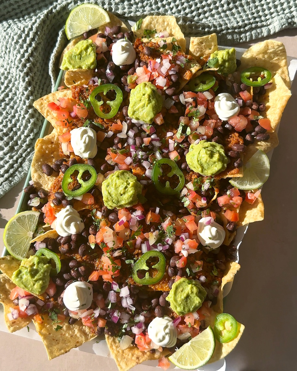 A colorful tray of nachos topped with chicken sausage, cheese, guacamole, and more.
