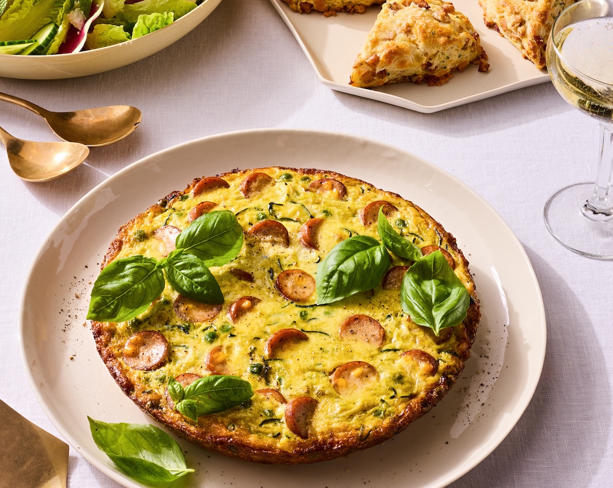A vibrant frittata on a table with scones and champagne.