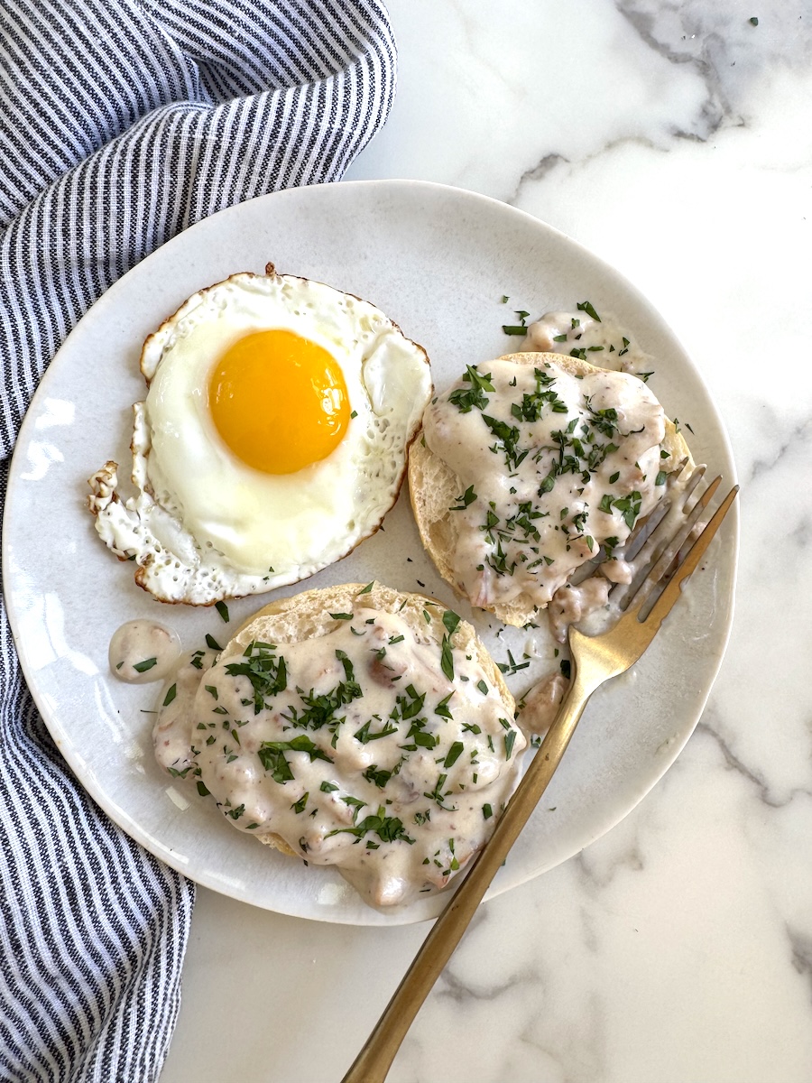 A partially eaten plate of chicken sausage biscuits and gravy with fried egg.