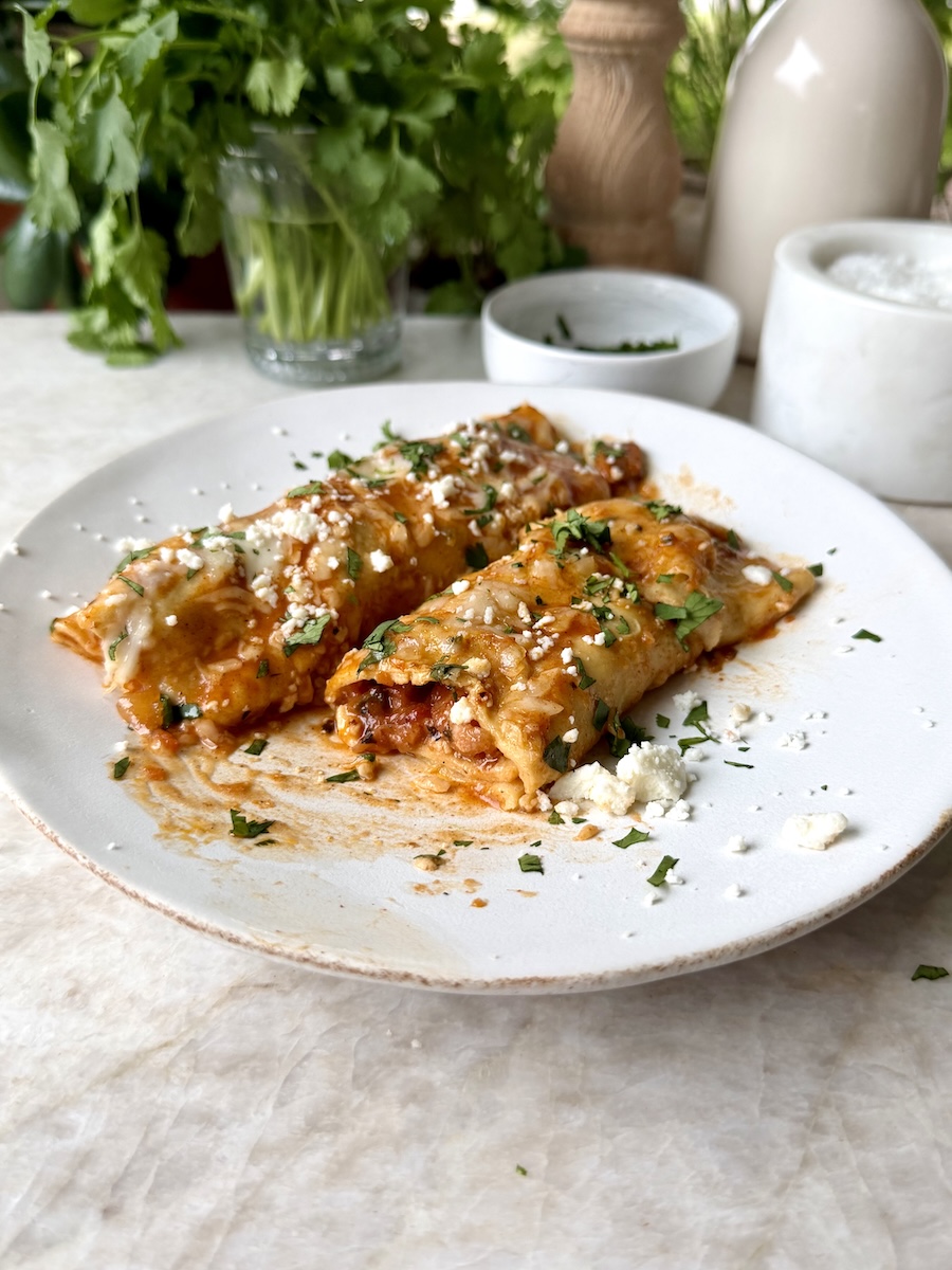 Two baked enchiladas cut in half on a plate.