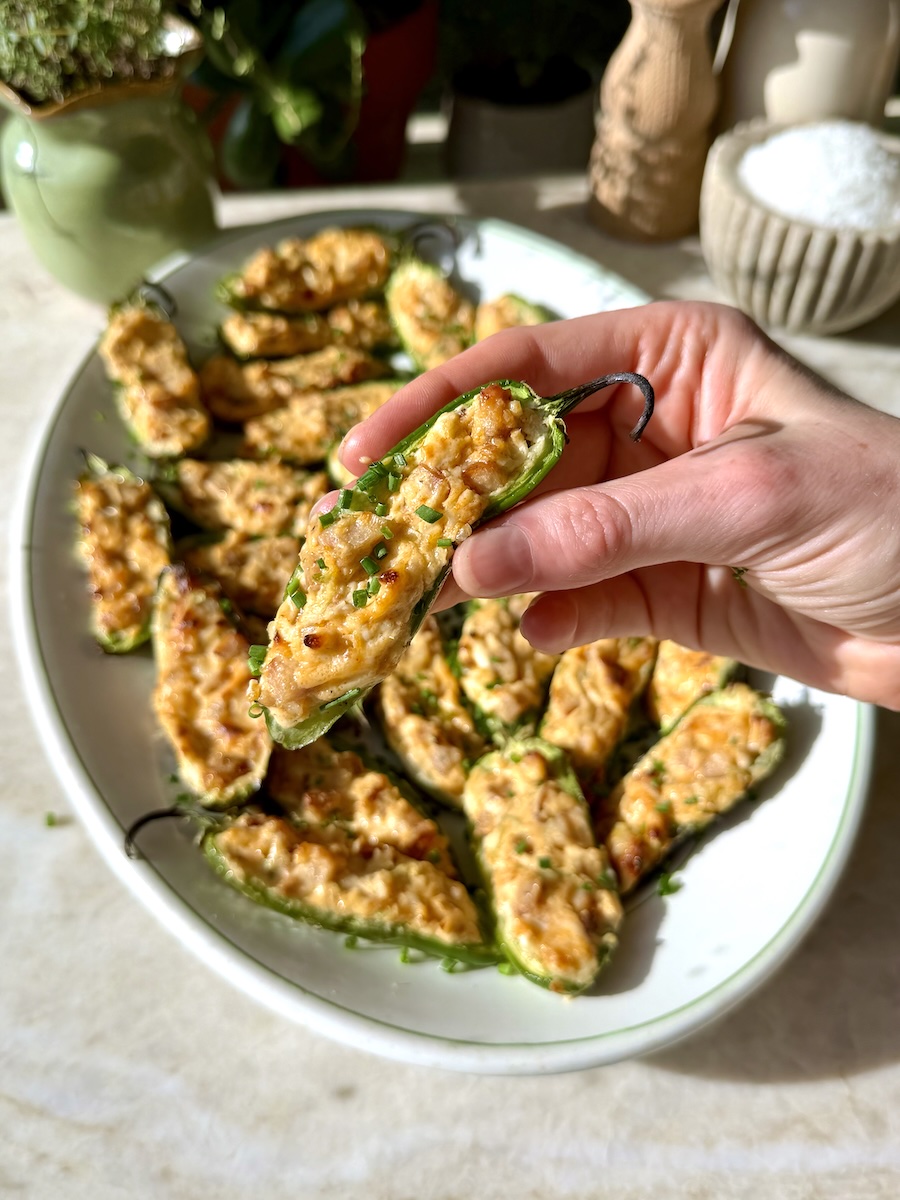 A hand holding a chicken sausage-stuffed jalapeño popper above a tray holding more appetizers.