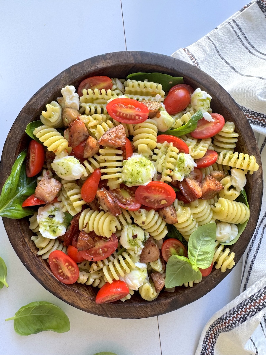 A heaping bowl of caprese pasta salad with fresh tomatoes, pesto, and Italian Herb Chicken Sausage.