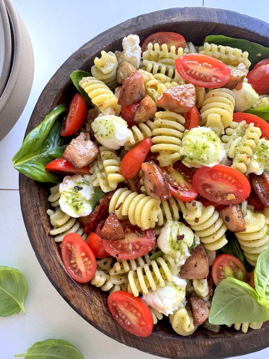 A bowl of caprese pasta salad with fresh tomatoes, pesto, and Italian Herb Chicken Sausage.