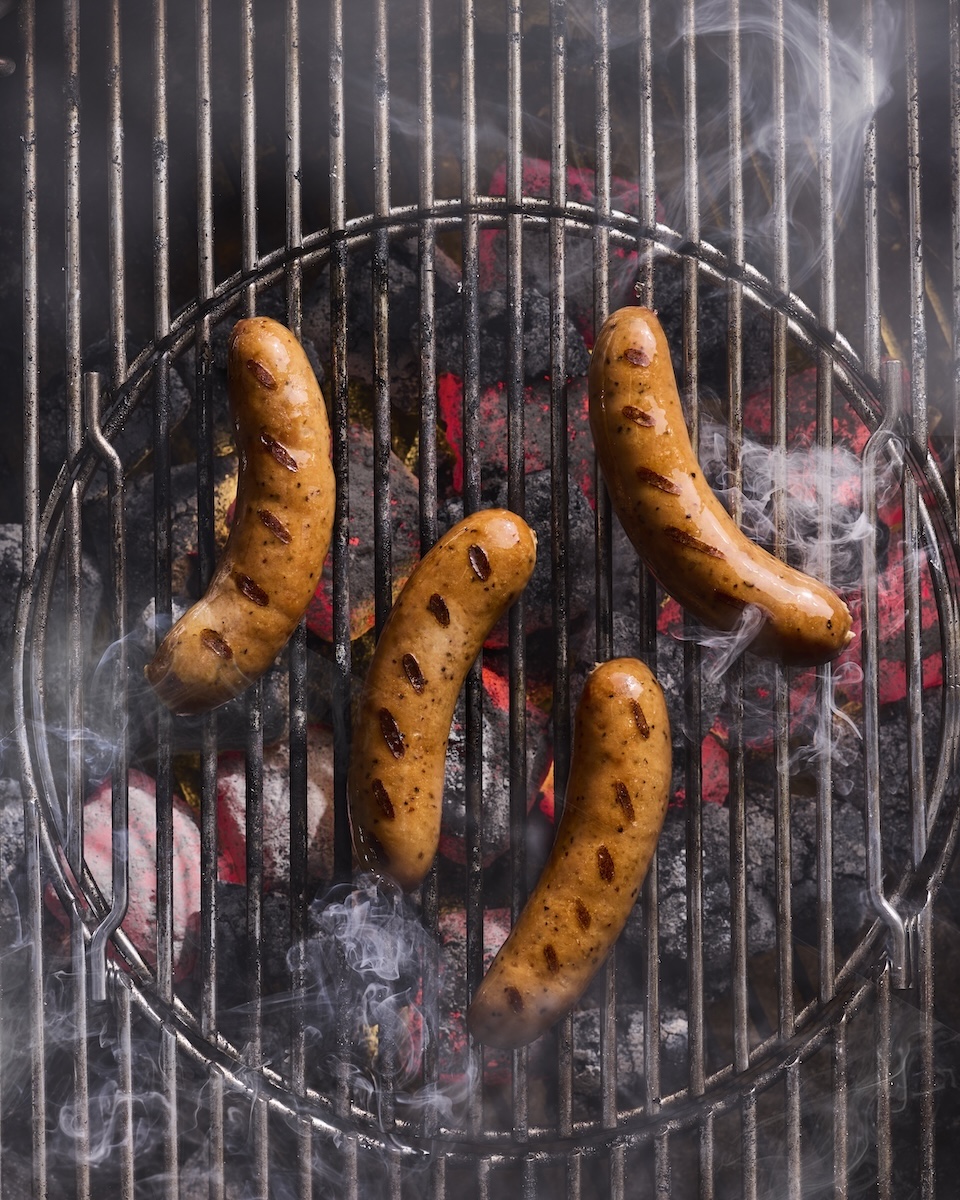 Four The Sausage Project chicken sausages on a smoky, smoldering grill.