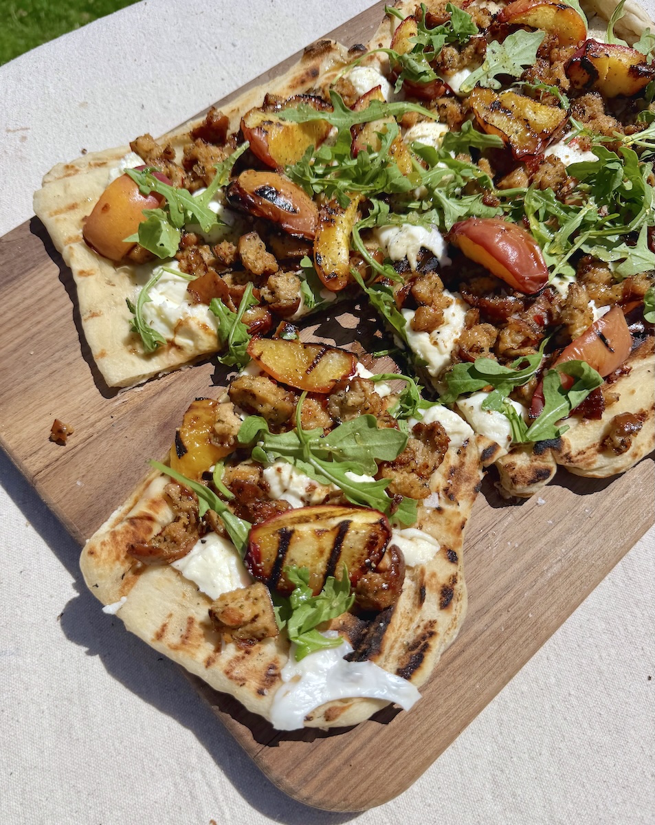 A grilled flatbread topped with cheese, chicken sausage, and grilled peaches.