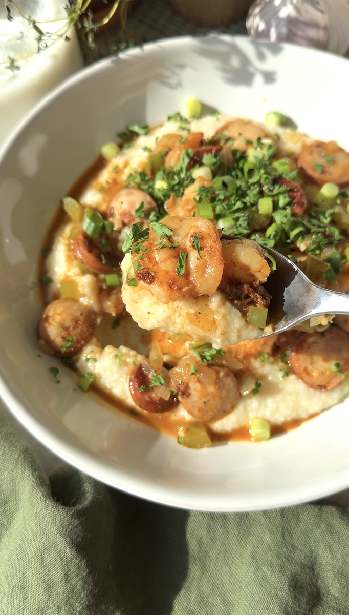 A bowl of cheesy shrimp & grits with chicken sausage.